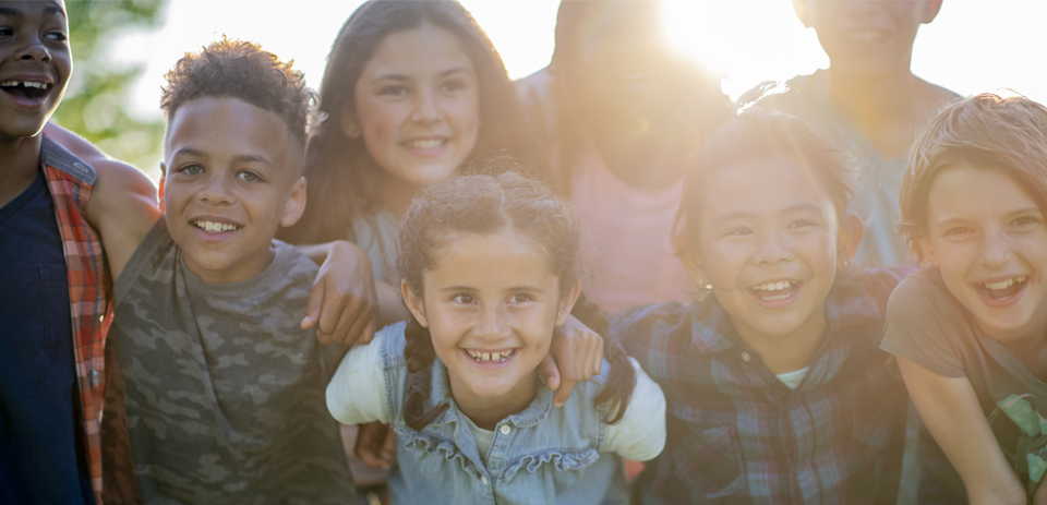 Image shows a group of children with their arms around each other smiling at the camera