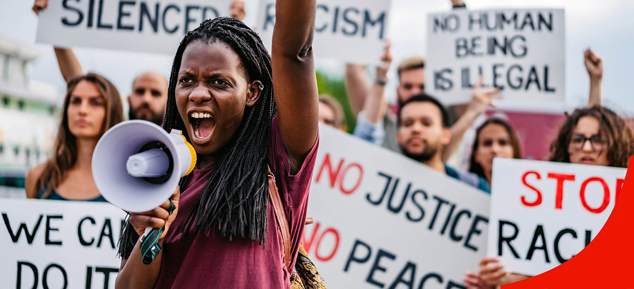 An image of a person with a megphone and a rallying crowd in the background. 