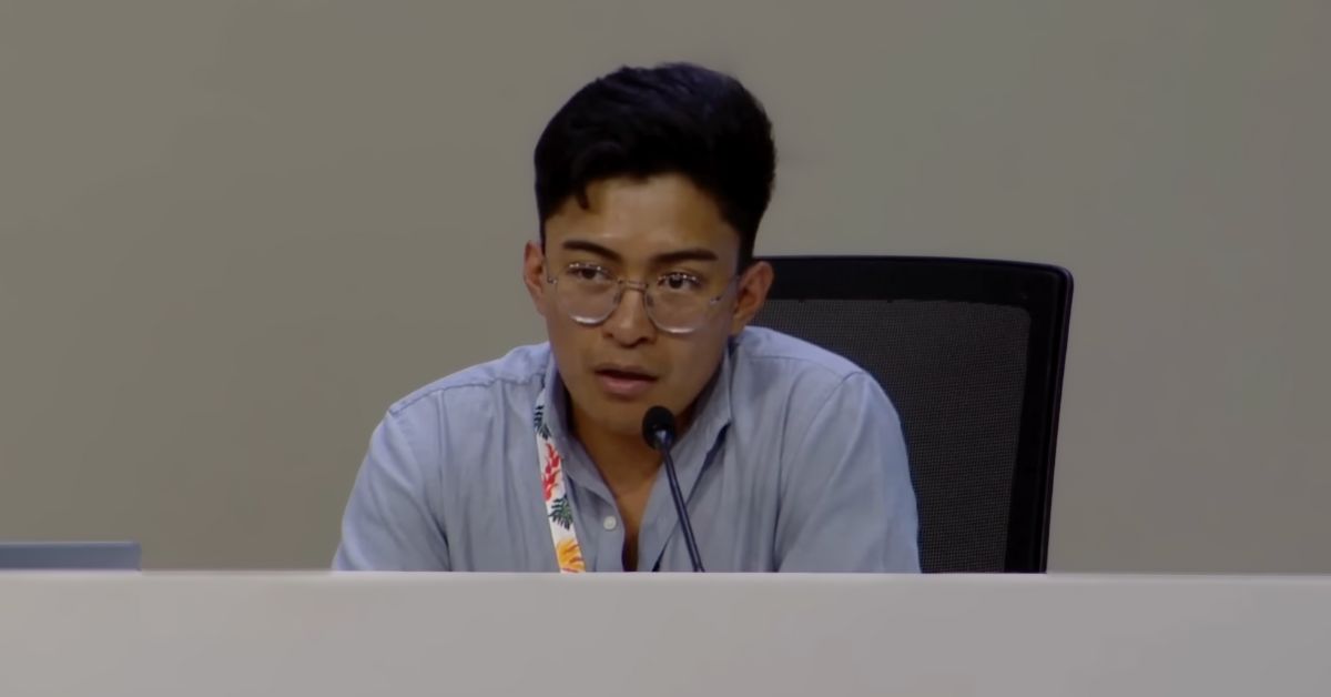 A young man speaking into a microphone at a conference panel.