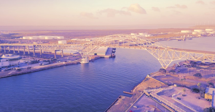 Aerial view of a bridge over water with oil storage tanks and industrial facilities in the background.