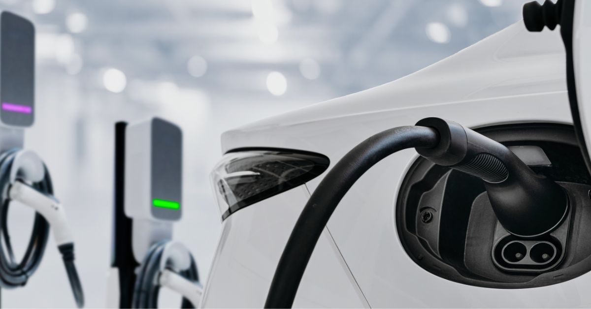 Electric vehicle charging cable connected to a white car at a charging station.