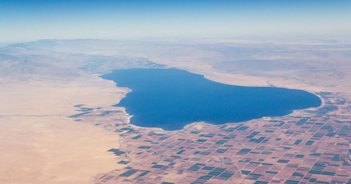 Aerial view of the Salton Sea, surrounded by desert and farmland, with distant mountains.