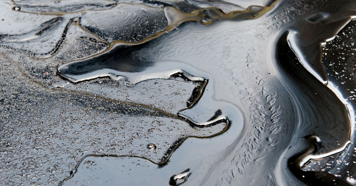 Close-up of dark, oily pollution spreading across a wet surface.