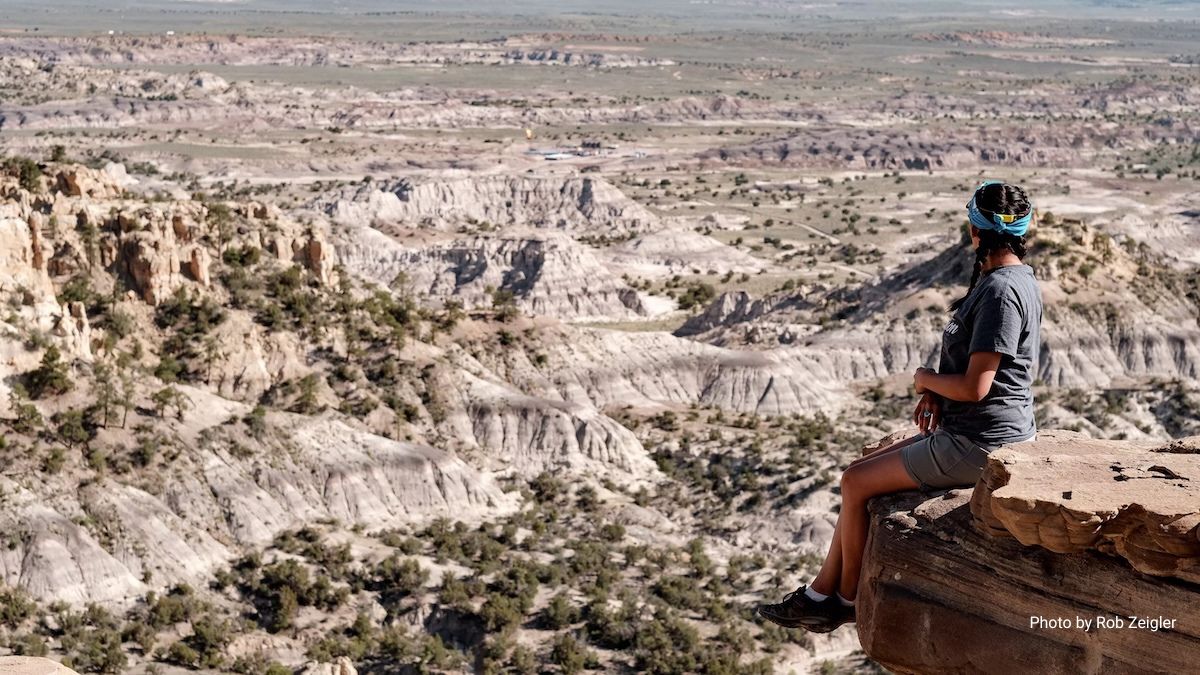 Diné activist and Earthworks Four Corners Indigenous Community Field Advocate Kendra Pinto sits on a high ledge near Twin Pines, New Mexico. In the distance, a well site emits a flare that can be seen and heard for miles. Photo by Rob Zeigler. 