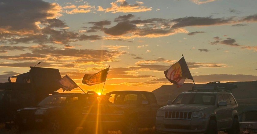 Vehicles with flags parked at sunset on a desert plain near Thacker Pass.