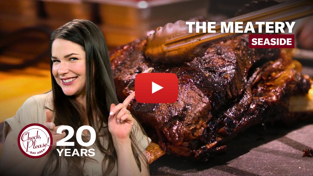 Woman smiling pointing to a plate of meat behind her.