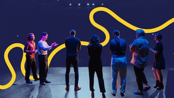 A group of storytellers applaud eachother on stage.