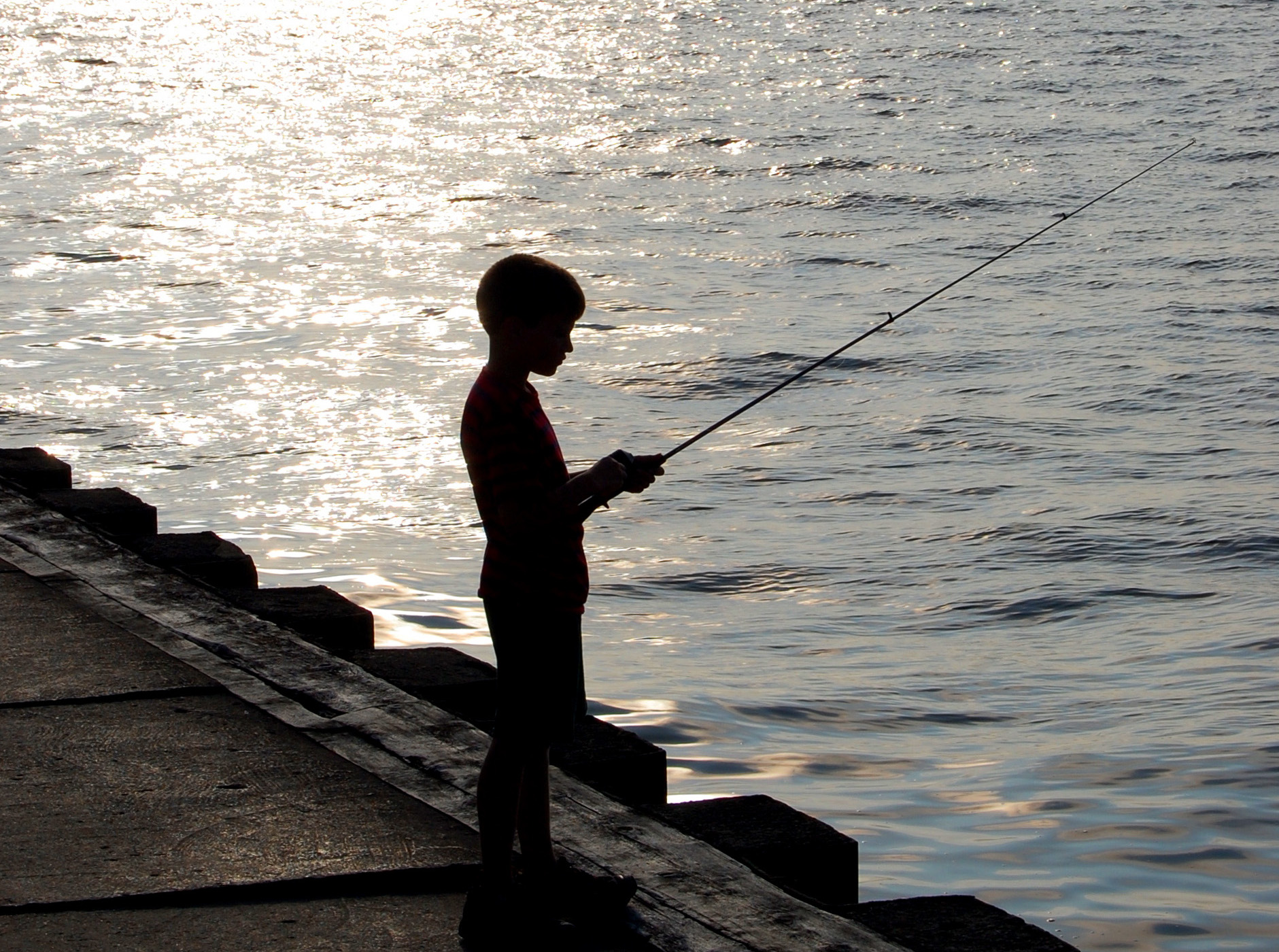 A boy fishes from a pier.