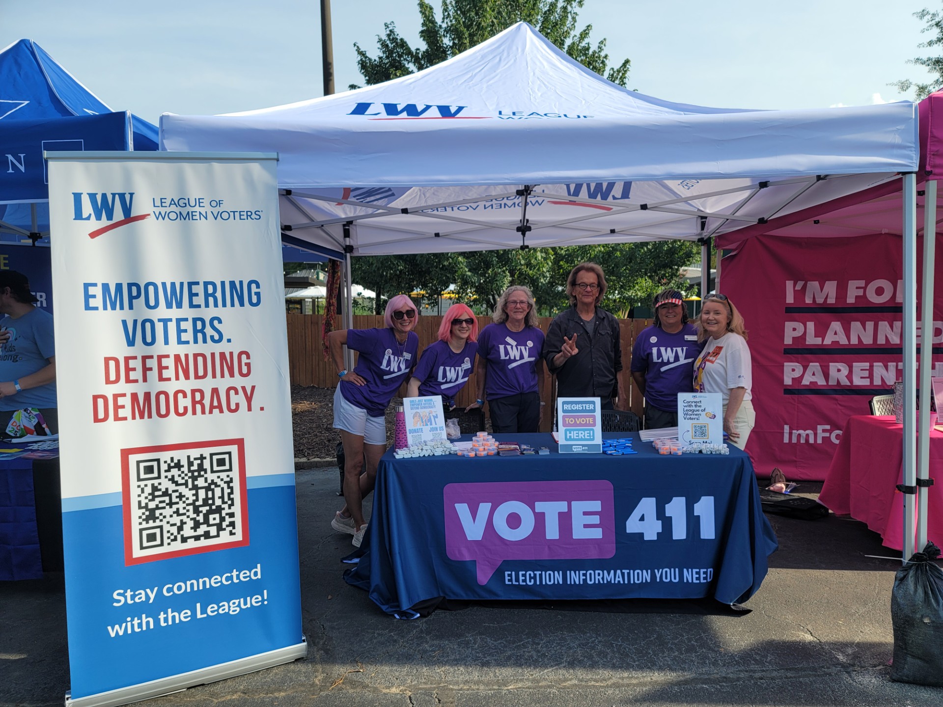 Photo of League volunteers and president Dianna Wynn tabling at a Cyndi Lauper concert. VOTE411 tablecloth and retractable banner that says EMPOWERING VOTERS DEFENDING DEMOCRACY Stay Connected wih the League!