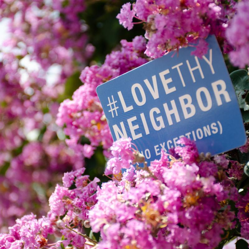 Love they Neighbor (no exceptions) sign in a flowering tree